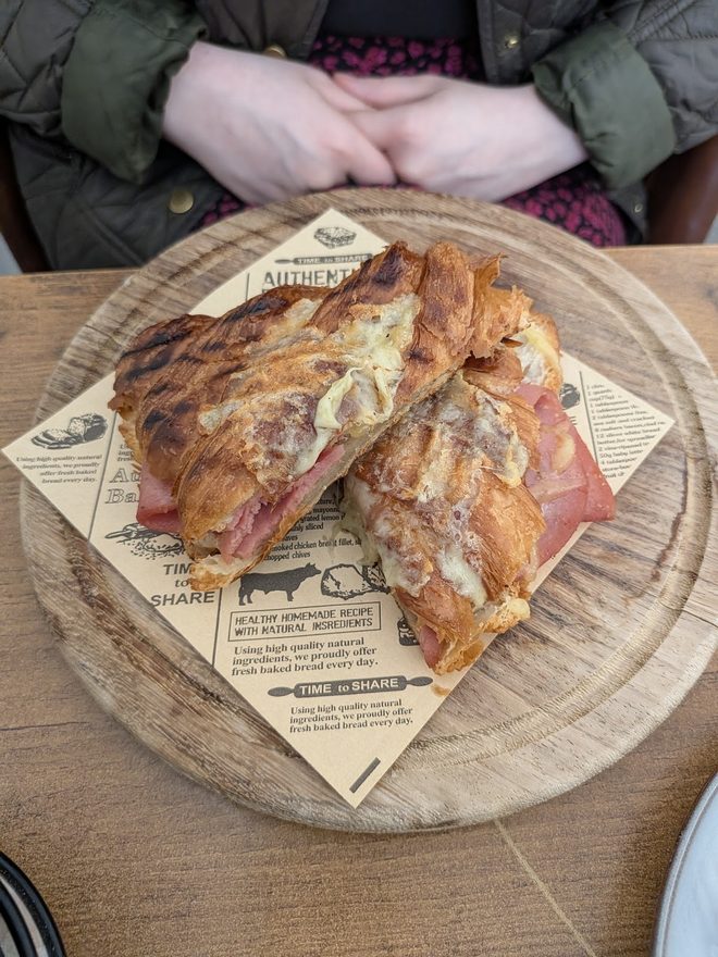 A toasted ham and cheese croissant halved on a wooden board