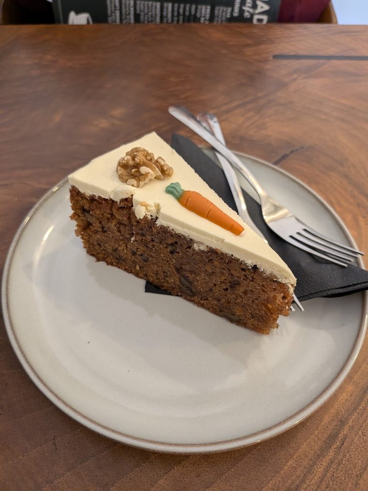 A slice of carrot cake with cream cheese frosting and a walnut on a grey plate